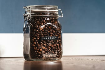 Sealed glass jar of whole coffee beans labeled espresso on a kitchen counter