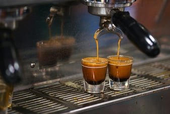 A double shot of espresso pouring from a portafilter into two glasses on an espresso machine