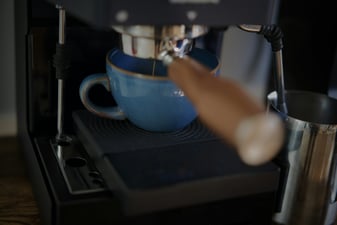 Espresso pouring from a portafilter into a blue ceramic cup at a home espresso machine