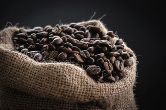 Freshly roasted specialty coffee beans spilling from an open burlap sack