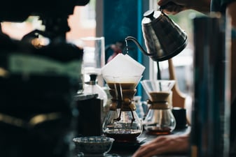 Hot water poured from a kettle into a pour over dripper over a glass coffee server