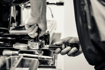 Barista tamping ground coffee in a portafilter with an espresso tamper