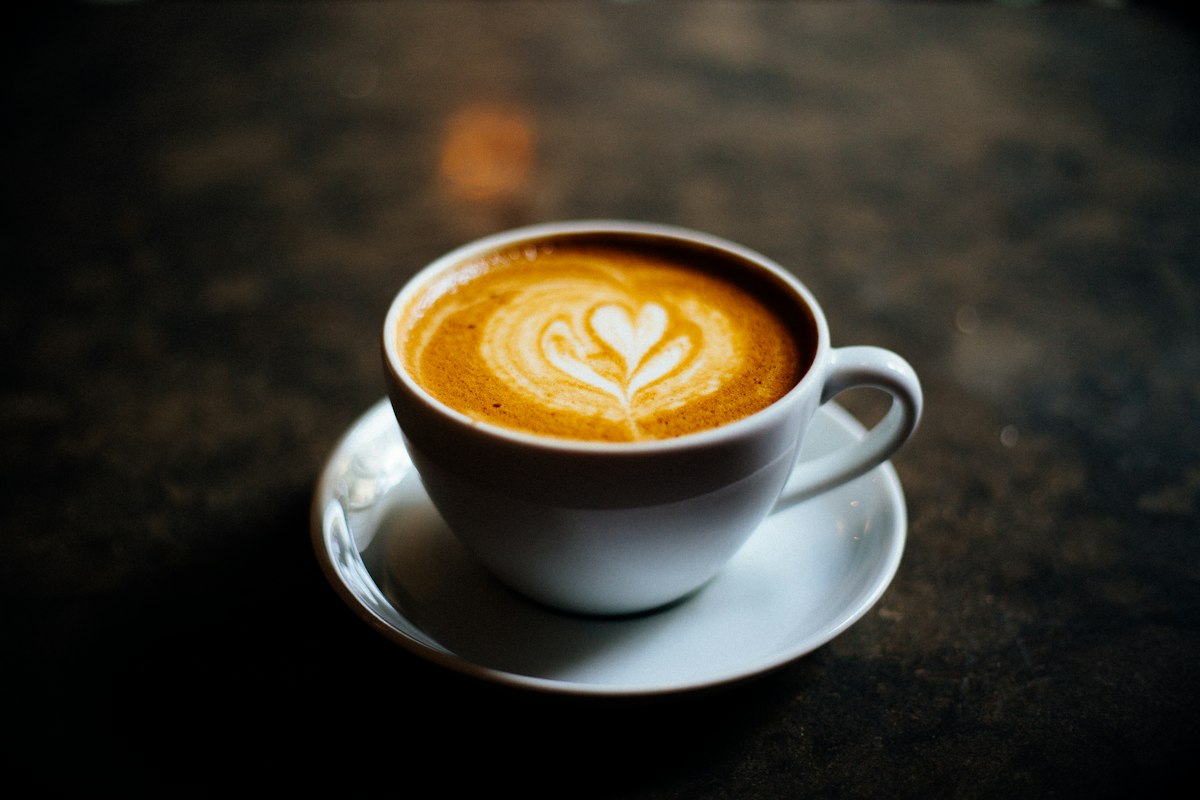 A cappuccino in a white cup with dense foam and latte art on a saucer