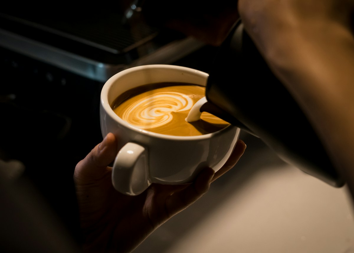 Steamed milk being poured from a frothing pitcher into a cappuccino cup