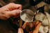 Hands holding a stainless steel pitcher while a steam wand textures milk for espresso