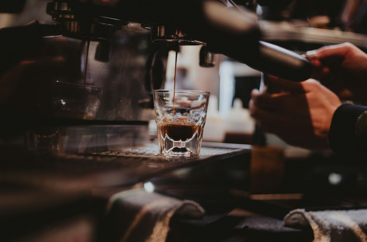 Espresso pouring from a portafilter into a small glass on an espresso machine