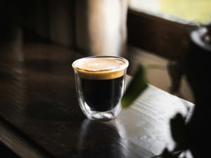 A short ristretto shot with heavy crema in a double-wall glass on a dark table