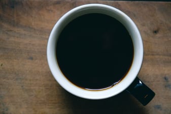 A cup of black coffee in a white and black ceramic mug on a walnut board