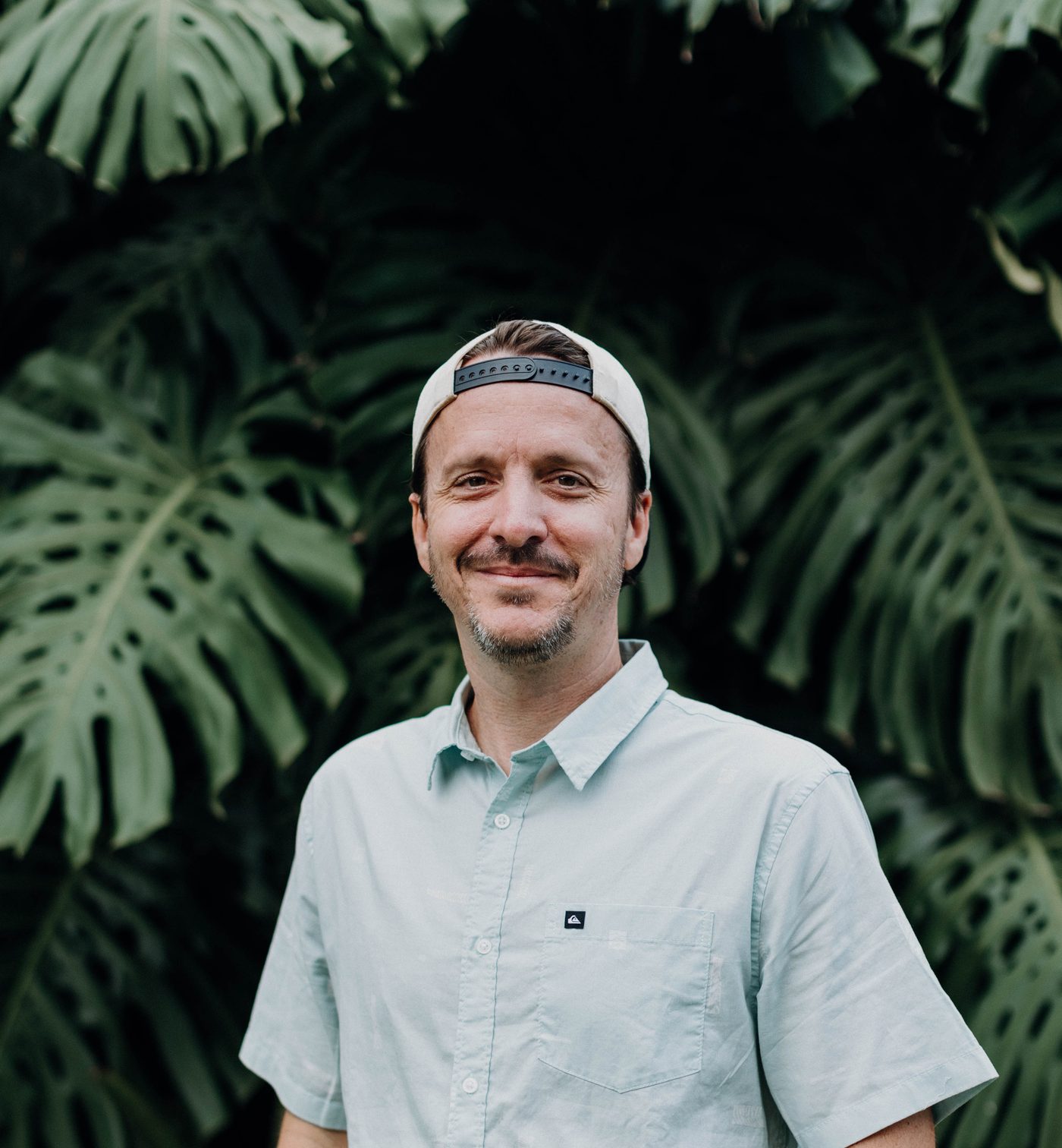 Daniel Norris smiling in a light blue button-down and backwards white cap, in front of monstera leaves