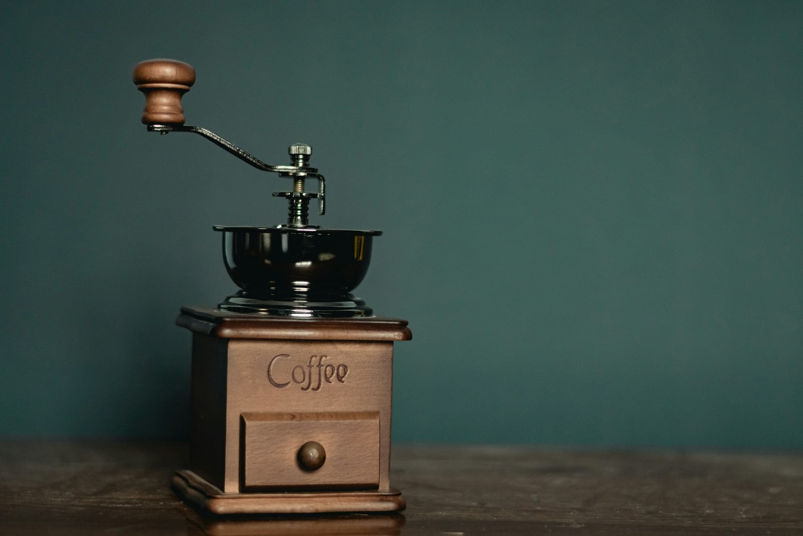 Wooden manual coffee grinder with a hand crank on a dark wood table